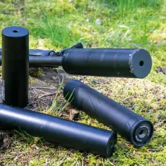 Tre ljuddämpare för jakt, en 125 mm, ligger på en mossig stubbe bredvid ett gevär. En guide hjälper dig att välja rätt.
