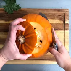 Händer skär i en halloweenpumpa på en skärbräda. Snart är den redo att bli en läskig dekoration!