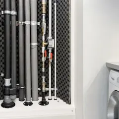 Rörsystem med ljuddämpning för ventilation, monterat bakom en dörr. Bredvid syns en tvättmaskin.
