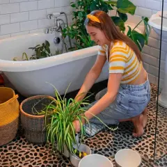 En ung kvinna vattnar blommor i badkaret, en mysig semesteraktivitet.