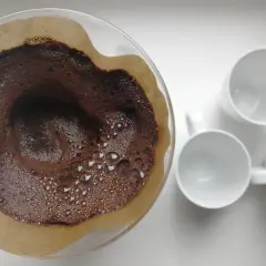 Kaffesump i filter, redo att användas som barriär mot sniglar i trädgården. Tre vita muggar står redo för kaffet.