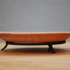 En terrakotta kruka, en av de stora krukfat, står på ett svart metallstativ på ett träbord.