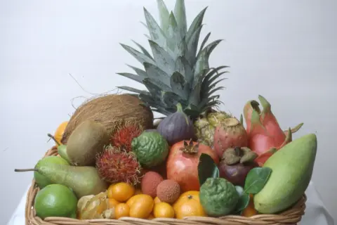 En korg fylld med exotiska frukter, inklusive en ananas som ser ut att vara redo att plantera.