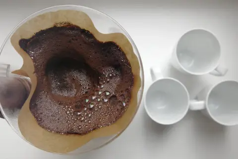 Kaffesump i filter, redo att användas som barriär mot sniglar i trädgården. Tre vita muggar står redo för kaffet.