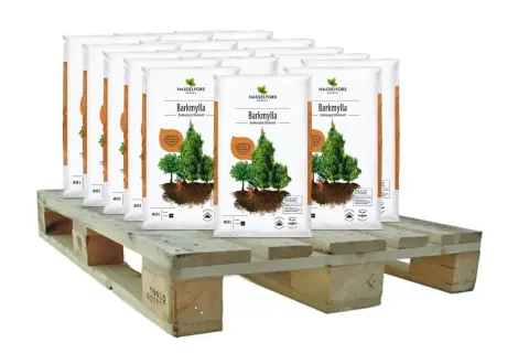 Sju säckar Barkmylla från Hasselfors Garden står på en träpall, redo att luckra upp jord och ge näring till dina växter.