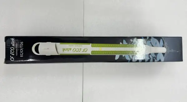 En vit ec mätare, CF ECO stick, ligger i sin svarta förpackning med gröna markeringar och bladmotiv.