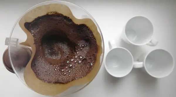 Kaffesump i filter, redo att användas som barriär mot sniglar i trädgården. Tre vita muggar står redo för kaffet.