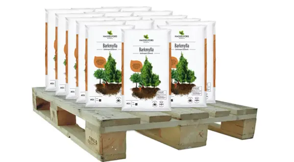 Sju säckar Barkmylla från Hasselfors Garden står på en träpall, redo att luckra upp jord och ge näring till dina växter.