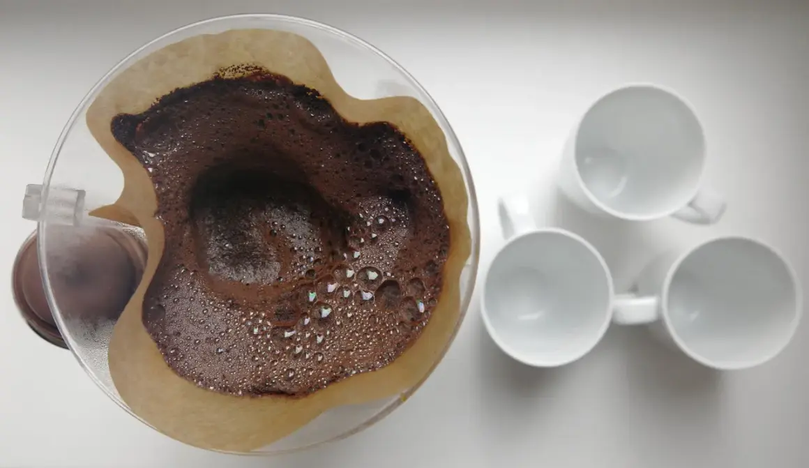 Kaffesump i filter, redo att användas som barriär mot sniglar i trädgården. Tre vita muggar står redo för kaffet.