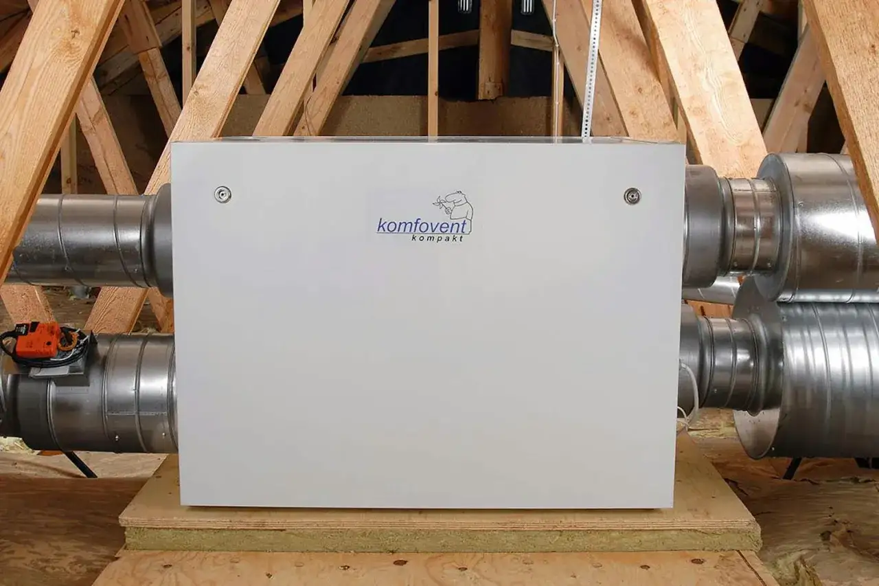 En Komfovent kompakt fl&auml;kt utsug installerad p&aring; en vind, med synliga ventilationsr&ouml;r och tr&auml;bj&auml;lkar.